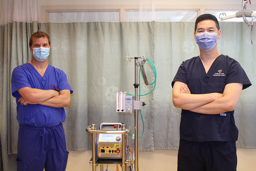 Dr. Marcelo Cypel (L) and Dr. Eddy Fan (R) with facemasks on, they are in scrubs in the hospital standing with their arms crossed 