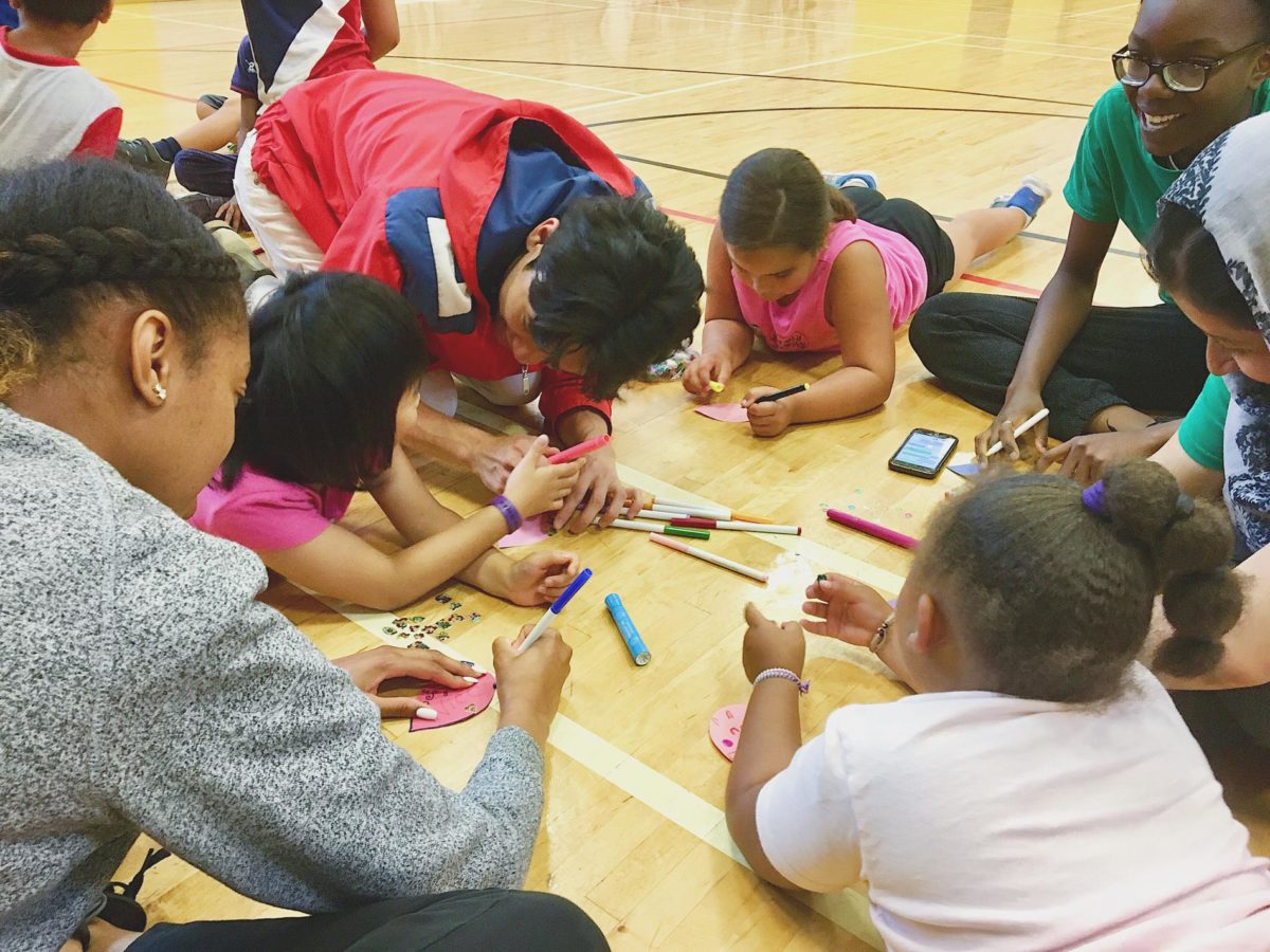 NEDIC volunteers with a group of kids in a school gym doing crafts