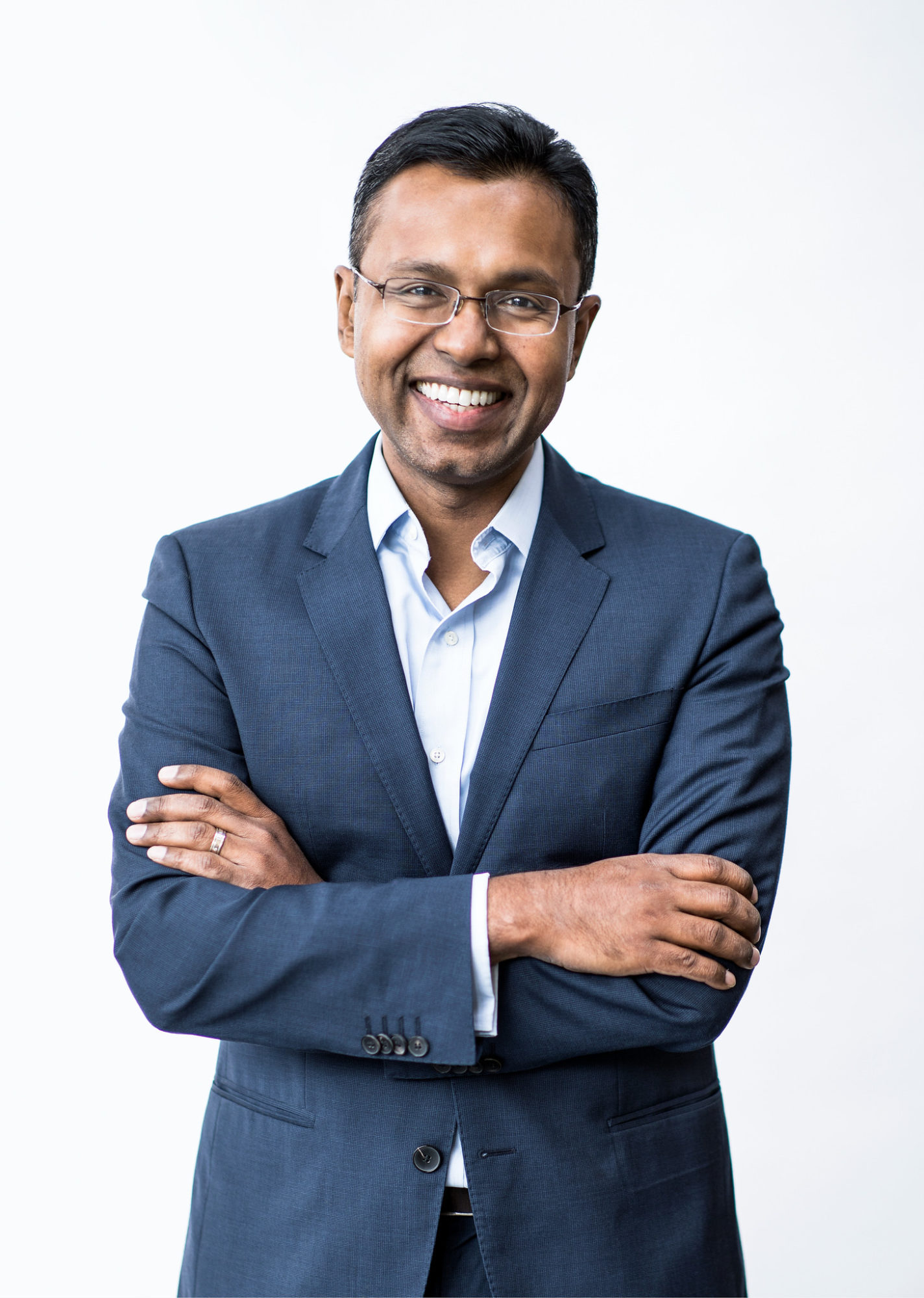 Dr. Dinesh Thavendiranathan smiling with a plain background. He is wearing a suit and his arms are crossed in front of him.
